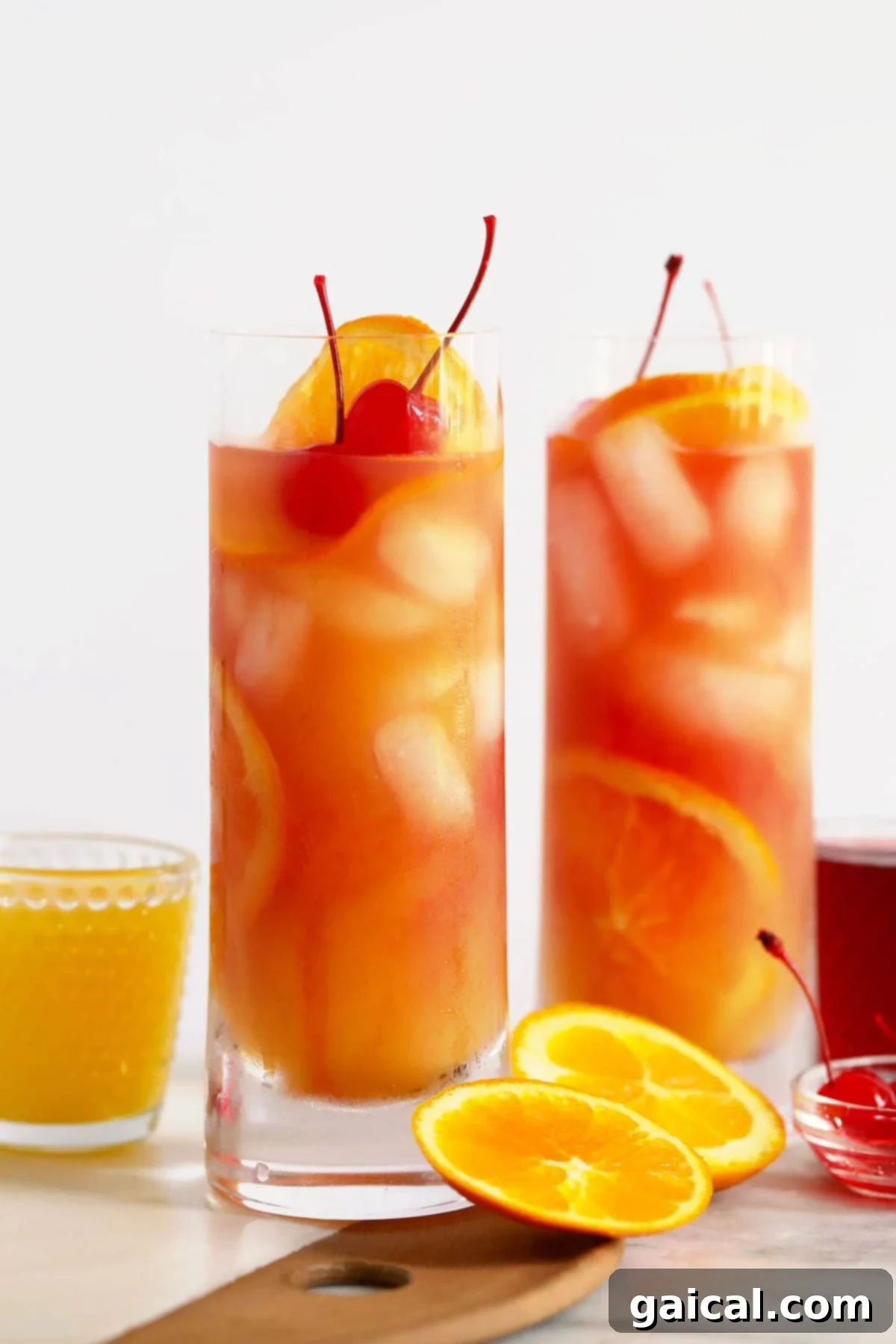 Two Sex on the Beach cocktails, garnished with fresh orange slices and maraschino cherries, sparkling in clear glasses.