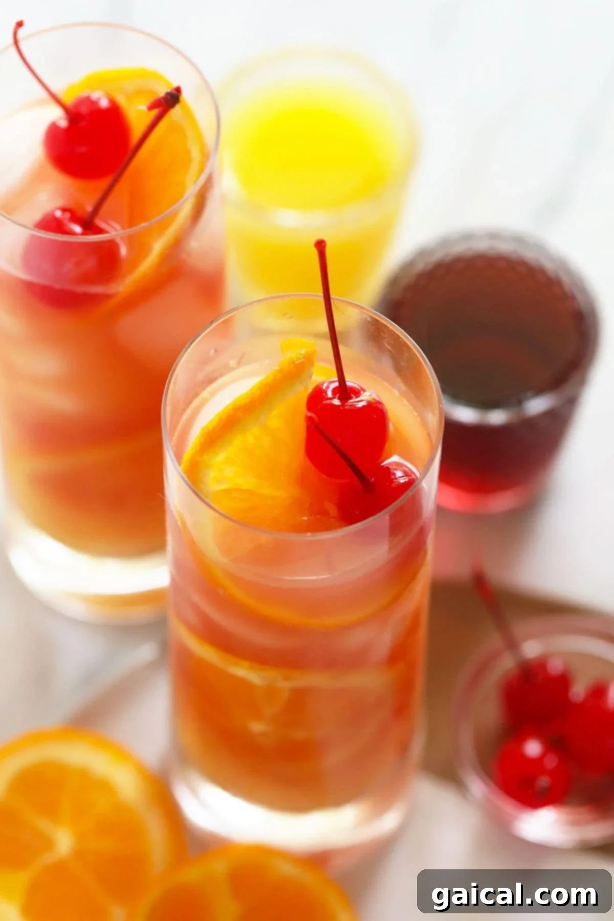 Two freshly made Sex on the Beach cocktails, garnished with cherries and oranges, sitting on a wooden surface.