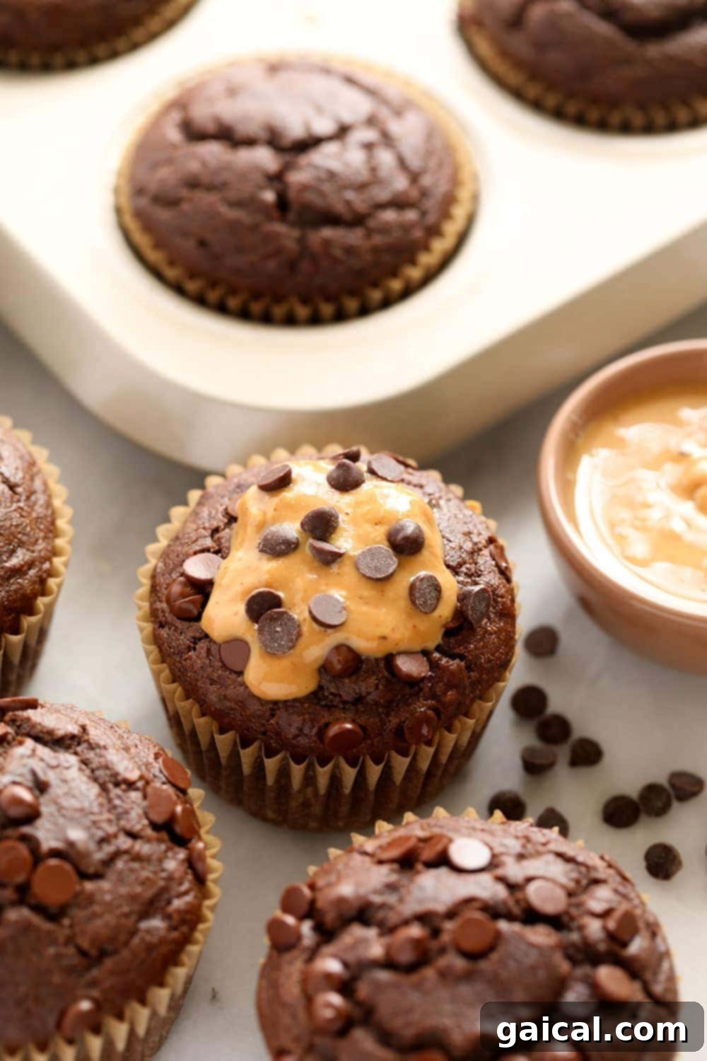 Incredibly moist healthy chocolate peanut butter muffins are made with whole wheat flour, naturally sweetened with coconut sugar and maple syrup, and flavored with all-natural peanut butter! Close-up of healthy chocolate peanut butter muffins with chocolate chips on top, stacked high and ready to eat.