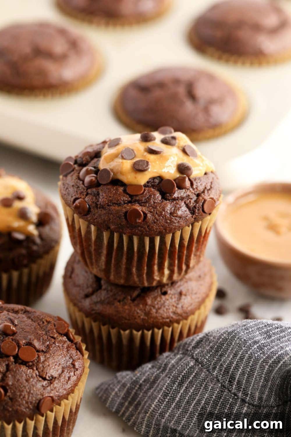 Incredibly moist healthy chocolate peanut butter muffins are made with whole wheat flour, naturally sweetened with coconut sugar and maple syrup, and flavored with all-natural peanut butter! A stack of perfectly baked healthy chocolate peanut butter muffins, showcasing their fluffy texture and chocolate chip topping.