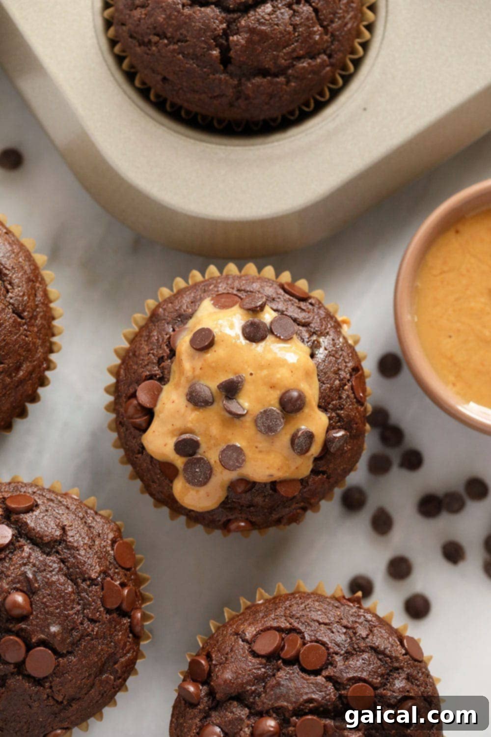 Incredibly moist healthy chocolate peanut butter muffins are made with whole wheat flour, naturally sweetened with coconut sugar and maple syrup, and flavored with all-natural peanut butter! Close-up of a single healthy chocolate peanut butter muffin, broken open to show its moist interior and melted chocolate chips and peanut butter swirls.
