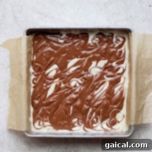 Cheesecake bars in a baking pan with the chocolate chai topping expertly swirled into the plain cheesecake layer.