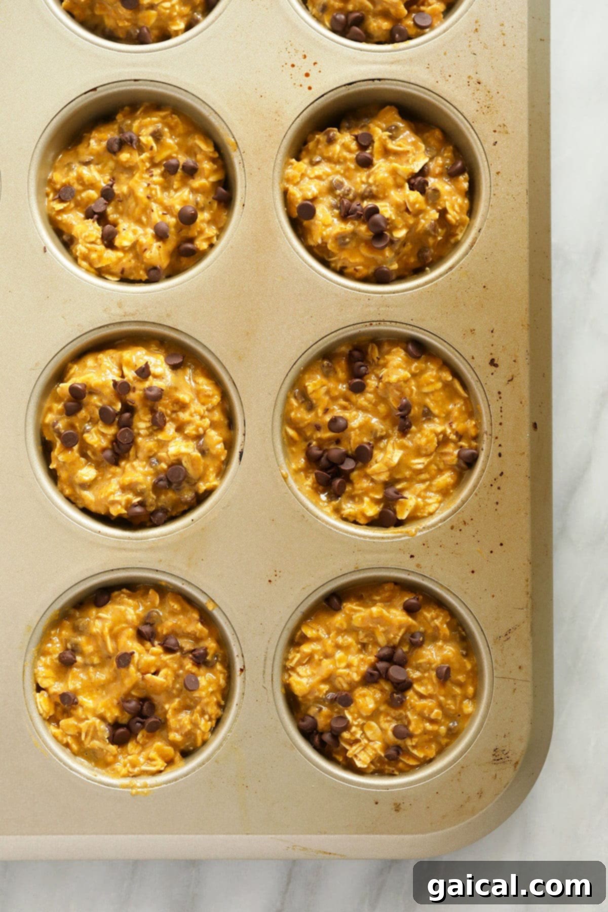 Spiced Pumpkin Oat Cups 3 Pumpkin oatmeal cups neatly arranged in a muffin tin, dotted with mini chocolate chips, ready to go in the oven.
