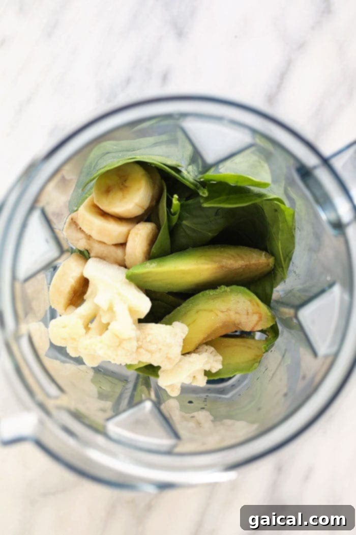 Try using a different kind of green in your green smoothie such as spinach, kale, or arugula! Various smoothie ingredients, including leafy greens and fruits, in a blender.