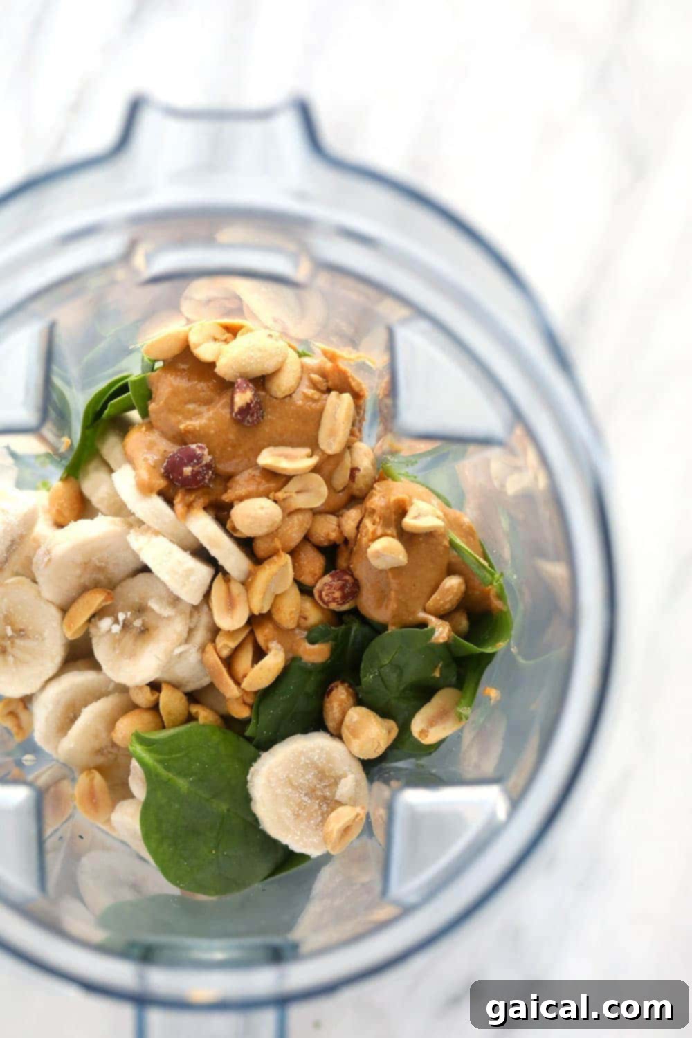 Have fun with your green smoothie recipe and add your favorite ingredients such as peanuts, peanut butter, and banana! A vibrant green smoothie topped with various ingredients.