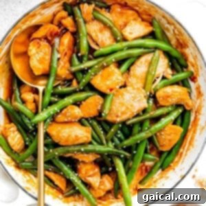 Kung Pao Chicken and green beans in a pan with sesame seeds.