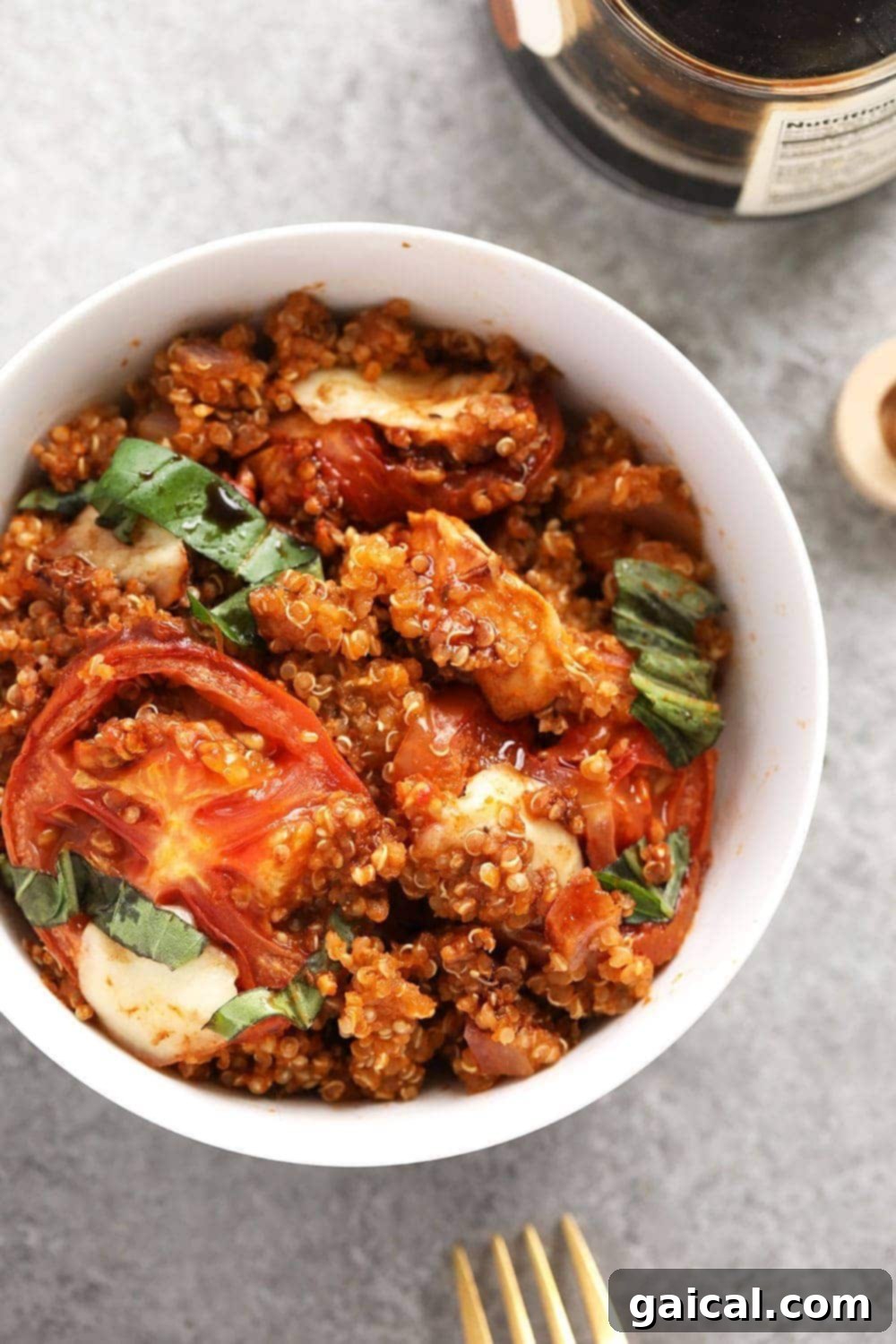 A close-up shot of a Tuscan Chicken Quinoa Bake in a white bowl, garnished with fresh basil, showcasing its rich tomato sauce, melted mozzarella, and tender chicken pieces.