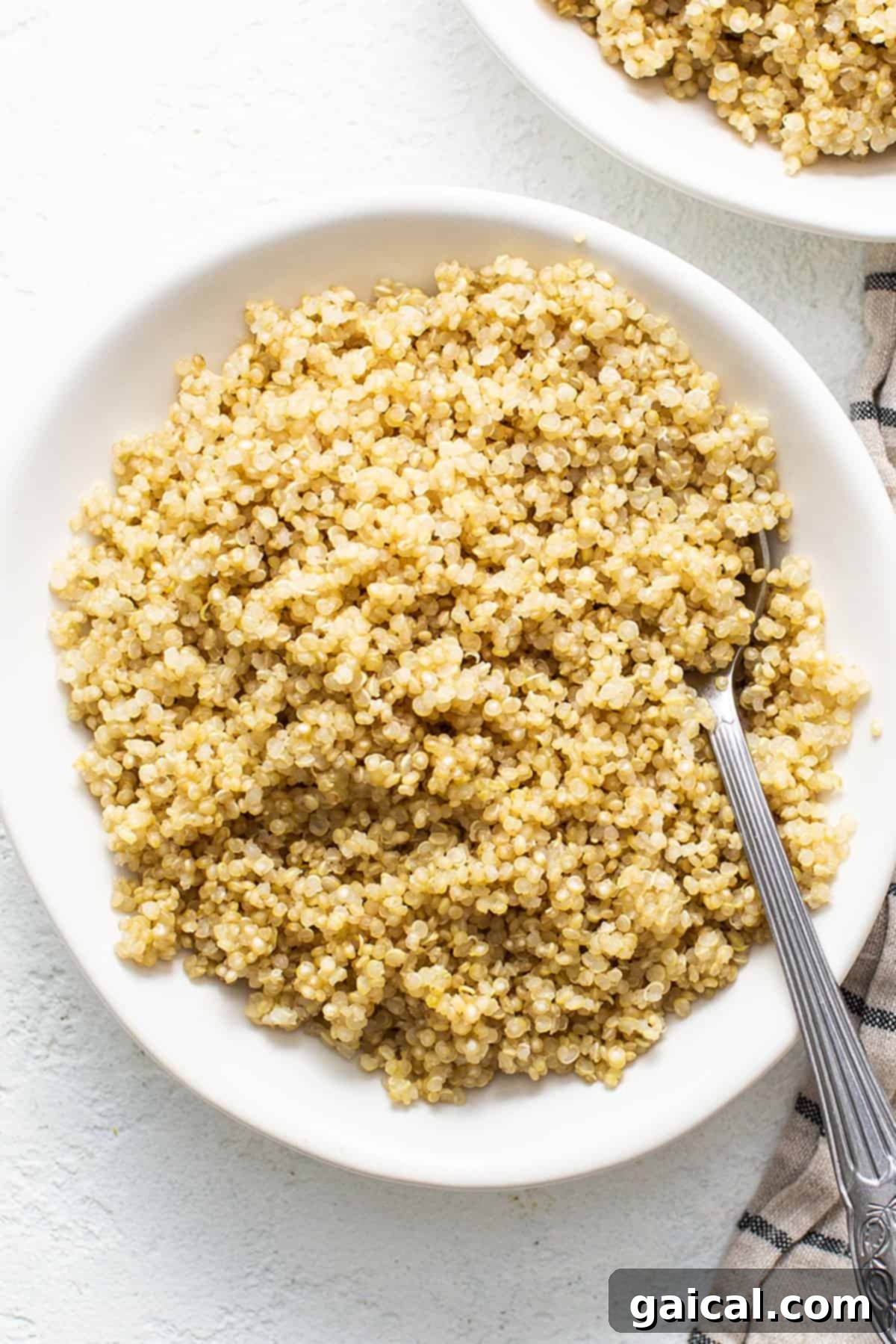 A white bowl filled with perfectly cooked quinoa, ready to be served, with a fork resting beside it.