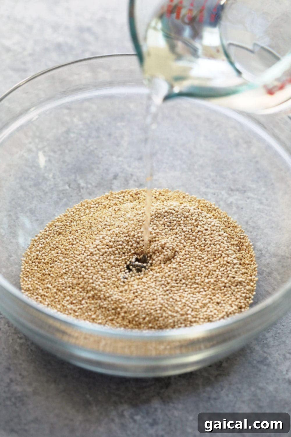 Uncooked white quinoa being rinsed in a bowl with water being poured over it.