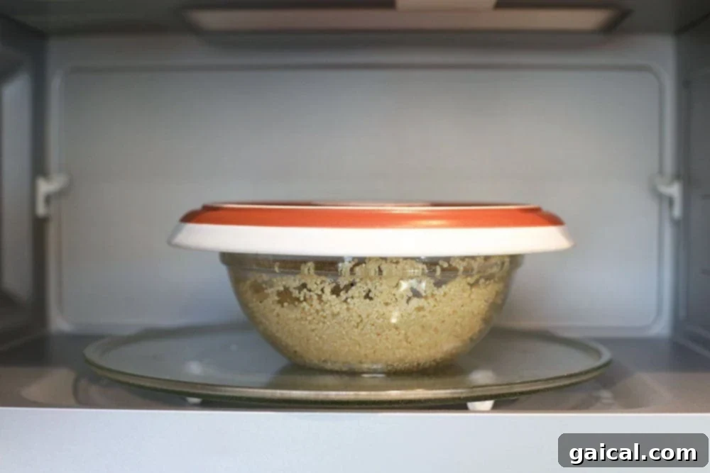 Quinoa in a deep, microwave-safe bowl with a plate covering it, placed inside a microwave oven.