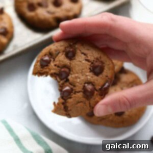 A hand holding a paleo cashew butter cookie with a bite taken out of it, showing the gooey interior.