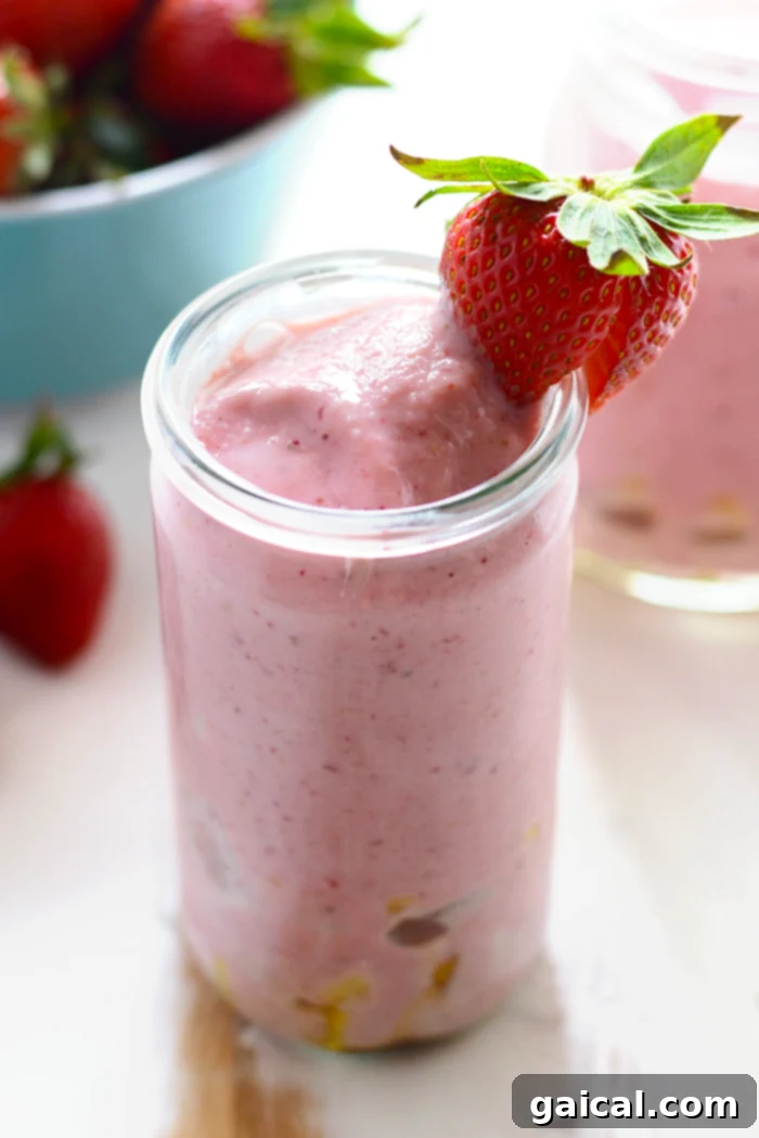 Thick Strawberry Pineapple Smoothie with Fresh Strawberry Garnish A vibrant strawberry pineapple smoothie in a glass with a strawberry on the rim, showcasing its thick and creamy texture.