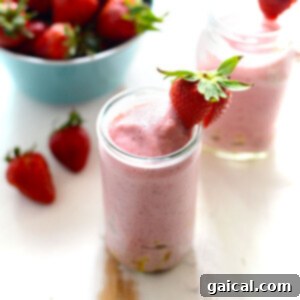 Strawberry pineapple smoothie with strawberry on rim of glass, served in a square dish.