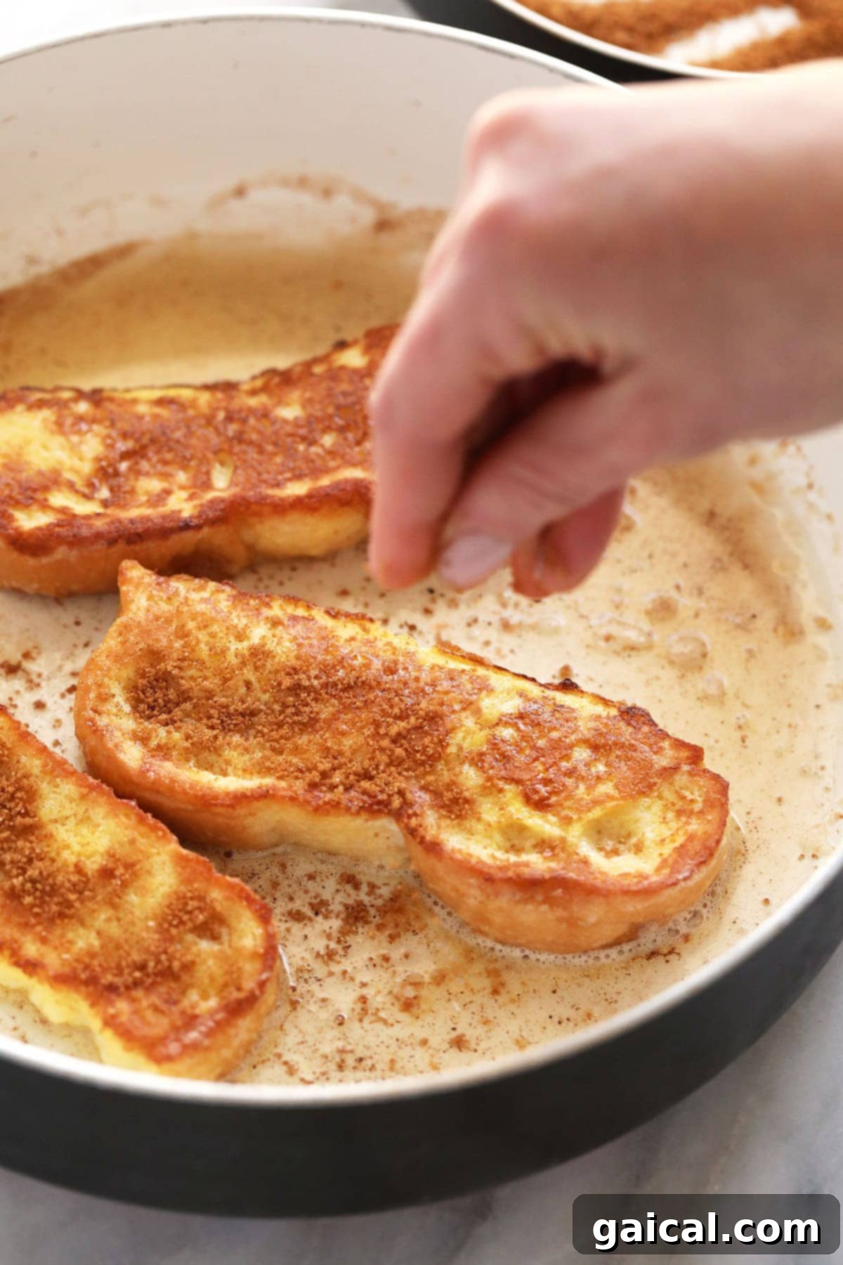 Generously sprinkling cinnamon sugar over freshly cooked French Toast Sticks in a hot pan for a delightful finish.