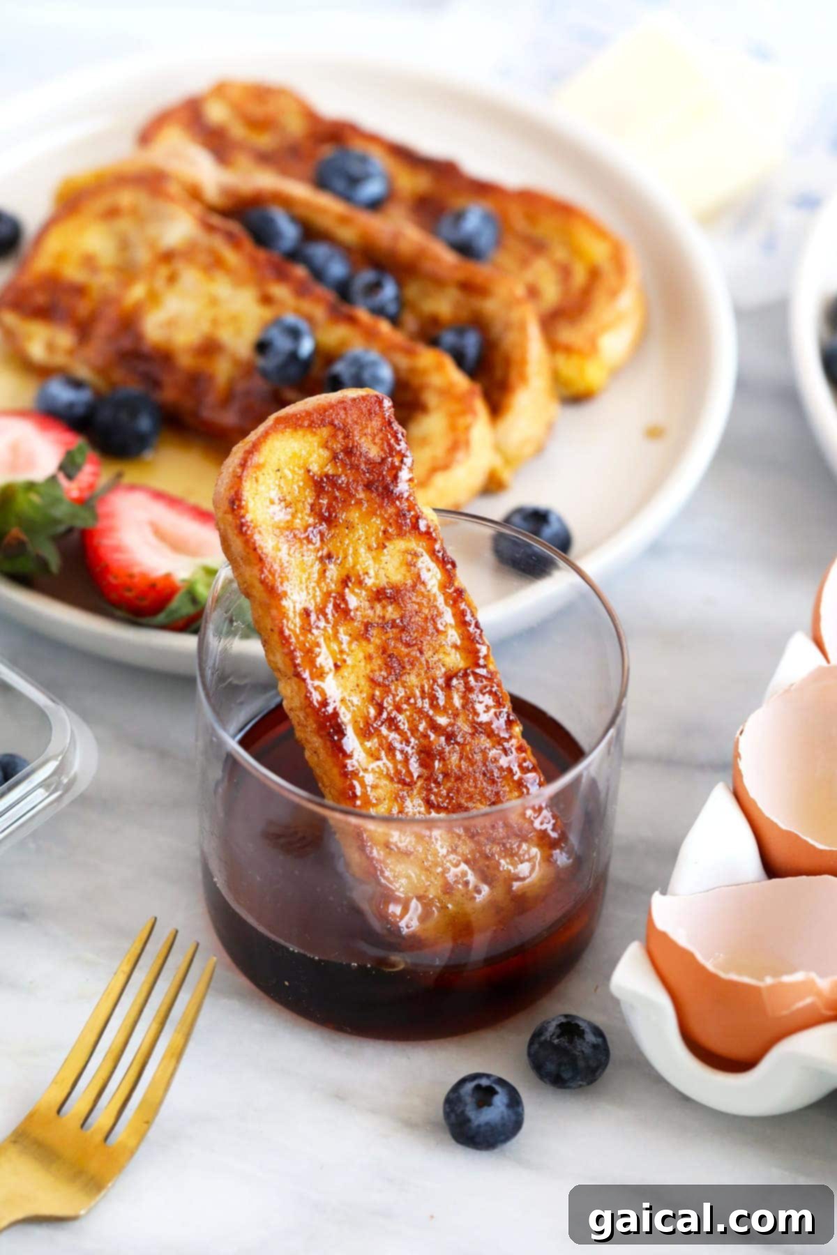 A single French toast stick being dipped into a small, inviting cup of golden maple syrup.