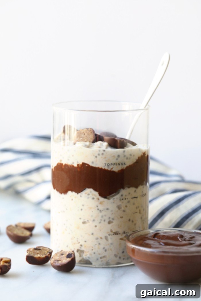 A glass jar filled with luscious Moose Tracks overnight oats, topped with chocolate chips and cookie dough pieces, ready for a delicious breakfast.