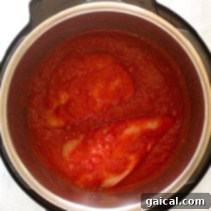Raw chicken breasts submerged in a vibrant buffalo-tomato sauce inside an Instant Pot, ready for pressure cooking.