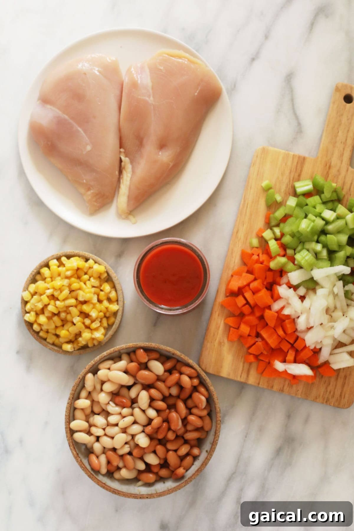 Zesty Instant Pot Buffalo Chicken Chili 3 Fresh ingredients for buffalo chicken chili laid out on a wooden cutting board, including diced vegetables, cans of beans, and spices.
