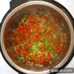 An Instant Pot filled with a colorful medley of chopped onions, carrots, and celery being sautéed.
