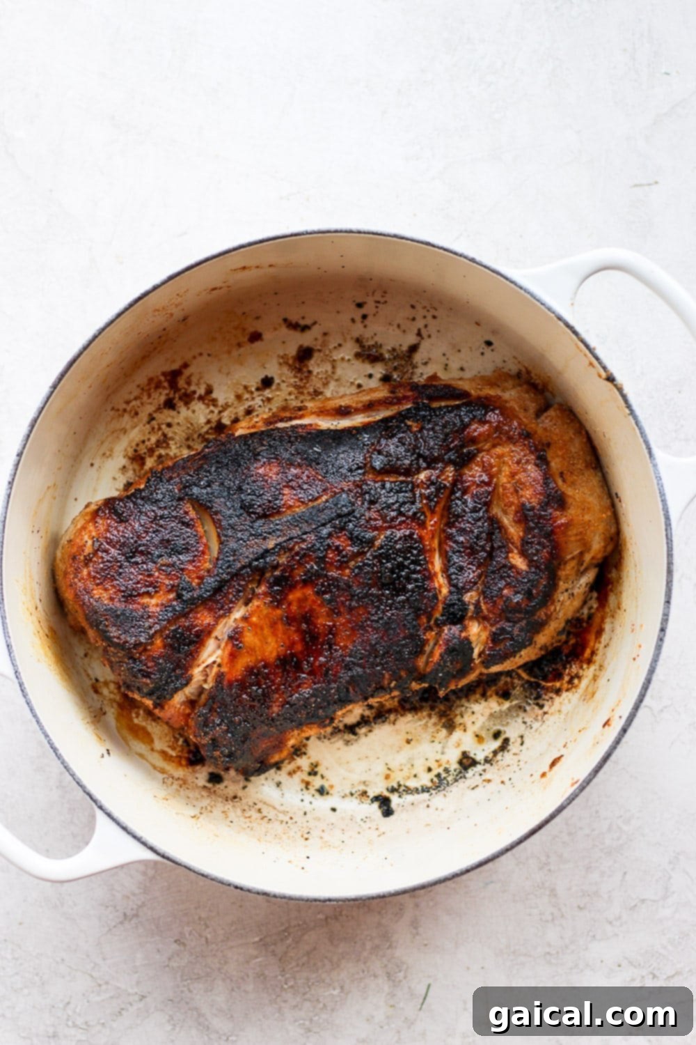 The best oven baked pork roast recipe made with tender potatoes and carrots served with a delicious savory gravy. Make this for dinner tonight! Seared pork shoulder resting in a sturdy cast iron stock pot, ready for the oven