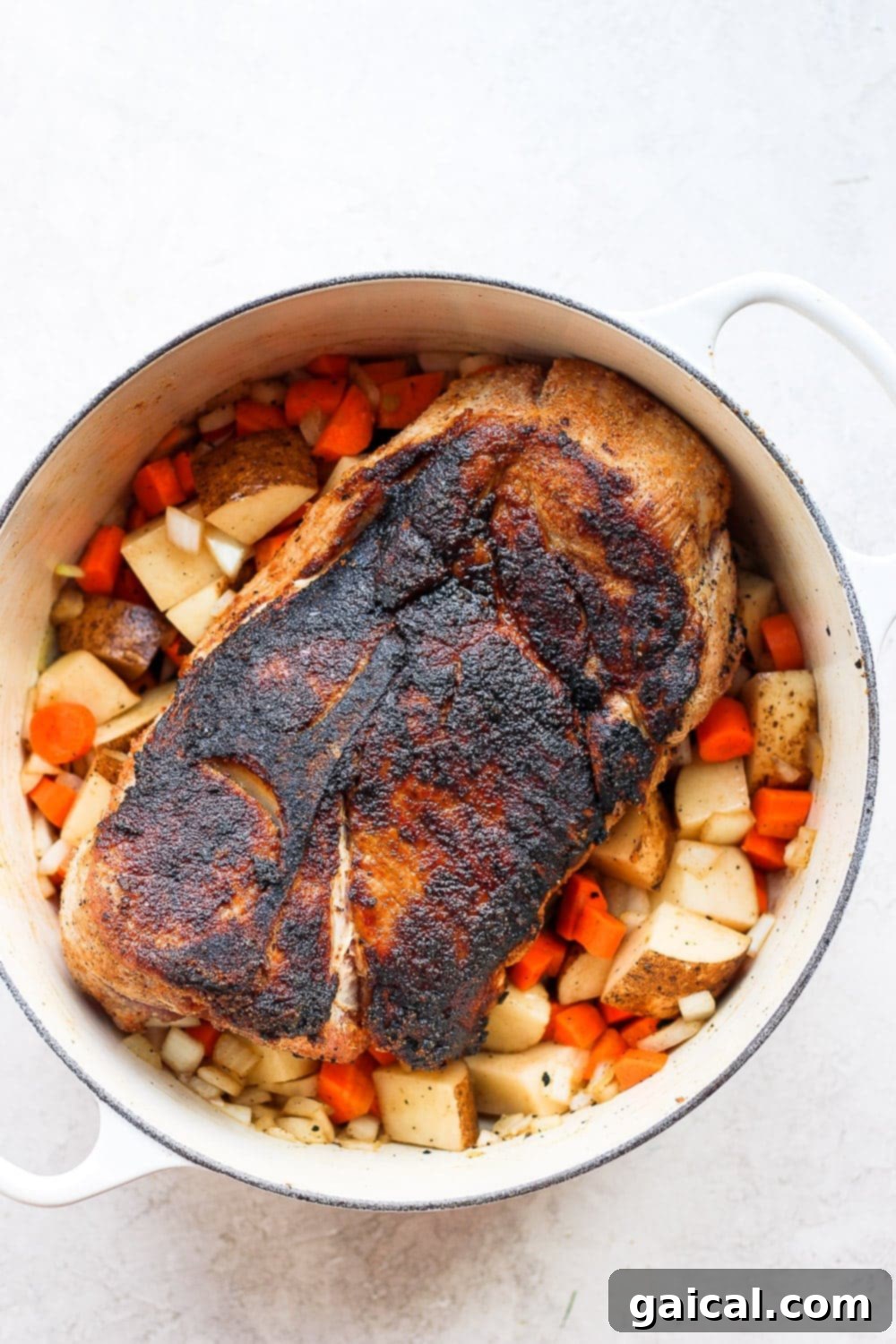 The best oven baked pork roast recipe made with tender potatoes and carrots served with a delicious savory gravy. Make this for dinner tonight! Pork shoulder nestled amidst a vibrant assortment of vegetables, poised for oven roasting