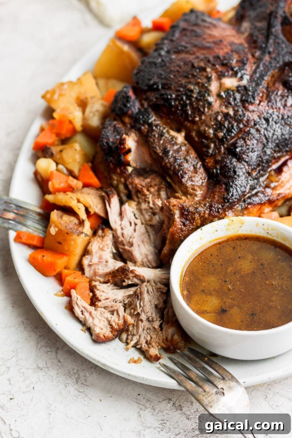 The best oven baked pork roast recipe made with tender potatoes and carrots served with a delicious savory gravy. Make this for dinner tonight! A perfectly cooked pork roast showcased on a serving platter, accompanied by roasted vegetables