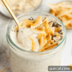 A glass jar filled with creamy coconut latte overnight oats, topped with toasted coconut flakes and chia seeds, with a gold spoon inserted.