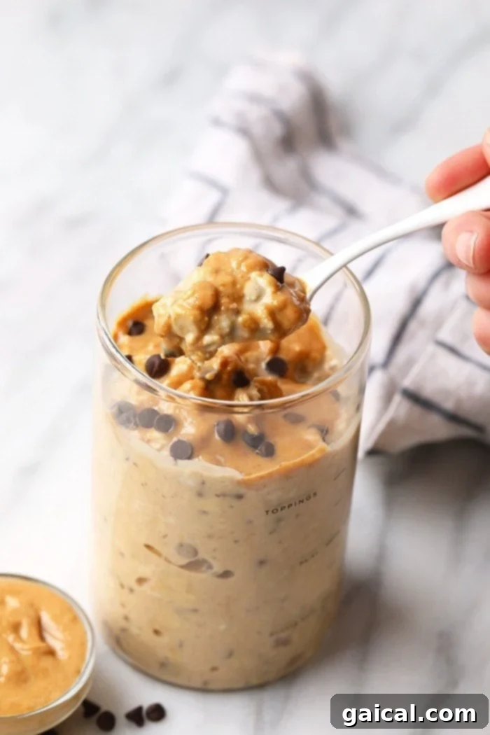 Enjoying a delicious spoonful of protein-packed overnight oats. A spoon lifting a creamy portion of peanut butter cookie dough overnight oats from a glass jar.