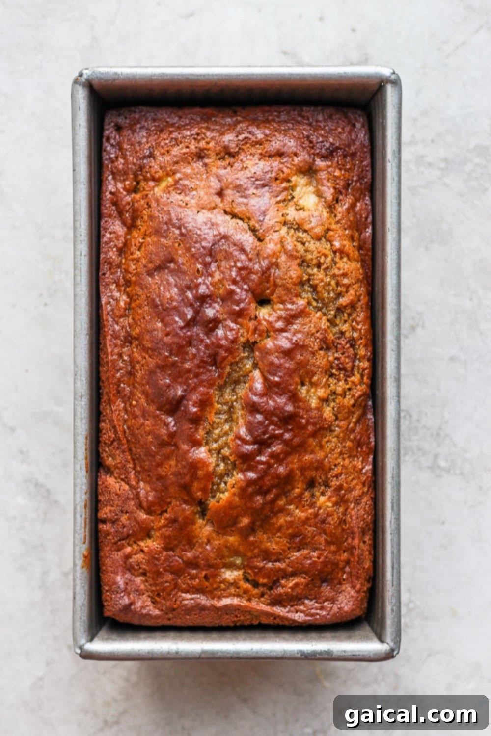 Delicious, airy, moist healthy banana bread coming right up! Our signature healthy banana bread recipe is made with white whole wheat flour, ripe bananas, all-natural sweeteners, and coconut oil. Freshly baked healthy banana bread in a loaf pan, cooling slightly before removal.
