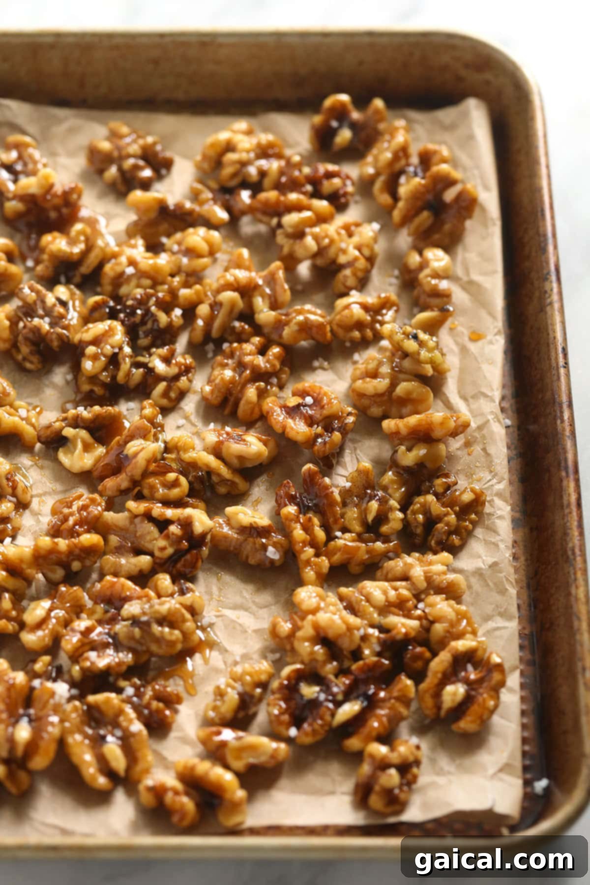 Looking for a last-minute Thanksgiving salad idea? Try our delicious massaged kale, apple, and walnut salad made with goat cheese, dried cherries, and our favorite vinaigrette! A baking sheet filled with golden-brown candied walnuts, some whole and some broken, cooling after being made.