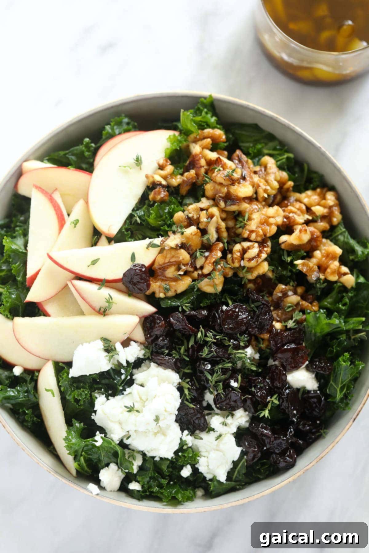 This flavorful Thanksgiving salad is made with massaged kale, sliced apple, candied walnuts, and goat cheese for a healthy side dish to share. A close-up of the Thanksgiving salad in a large wooden bowl, garnished with whole green leaves and a few scattered apple slices, ready for serving.