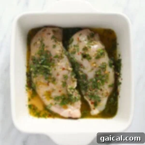 Two perfectly marinated Italian chicken breasts in a white baking dish, garnished with fresh herbs, ready for cooking.