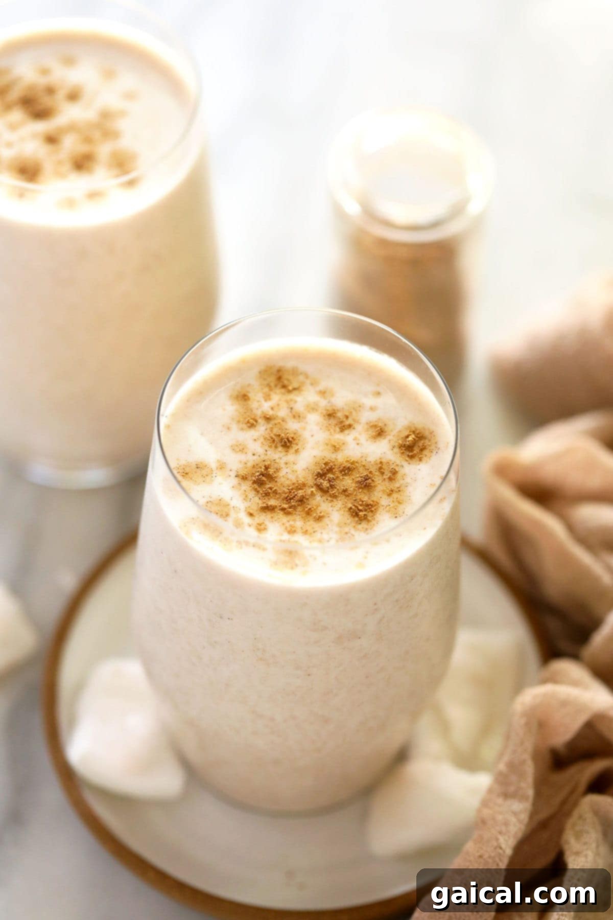 Spiced Coconut Protein Bliss 2 Two elegant glasses filled with creamy coconut chai protein shakes, garnished with a light sprinkle of chai spice on top. A healthy, inviting beverage.