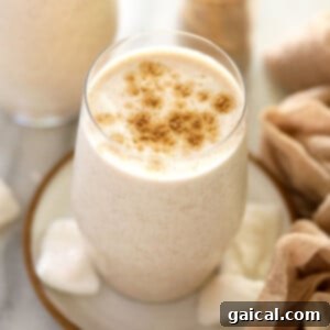A refreshing Coconut Chai Protein Shake served in a clear glass with a straw, garnished with a light sprinkle of spice.