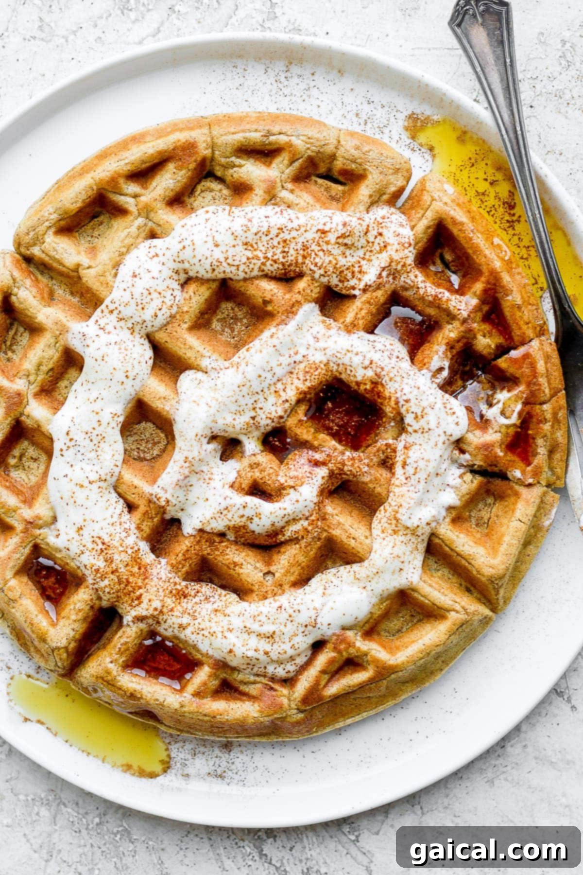 Waffled Cinnamon Rolls 6 A single healthy cinnamon roll waffle on a white plate, elegantly topped with a swirl of Greek yogurt cream cheese drizzle and a side of maple syrup for a delightful breakfast.