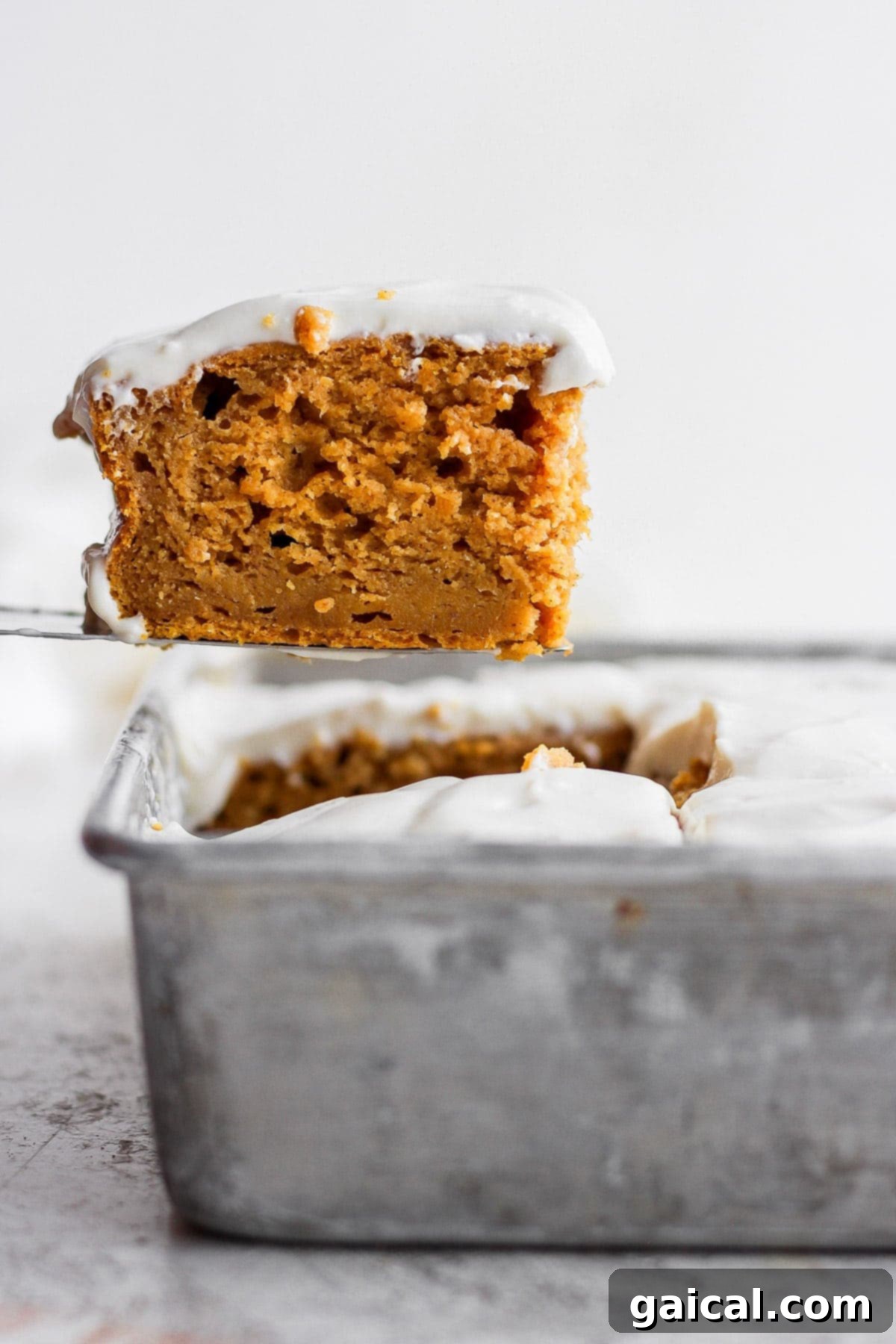Sheet Pan Pumpkin Perfection 6 A metal spatula lifting a piece of pumpkin sheet cake from the pan, revealing its moist texture.
