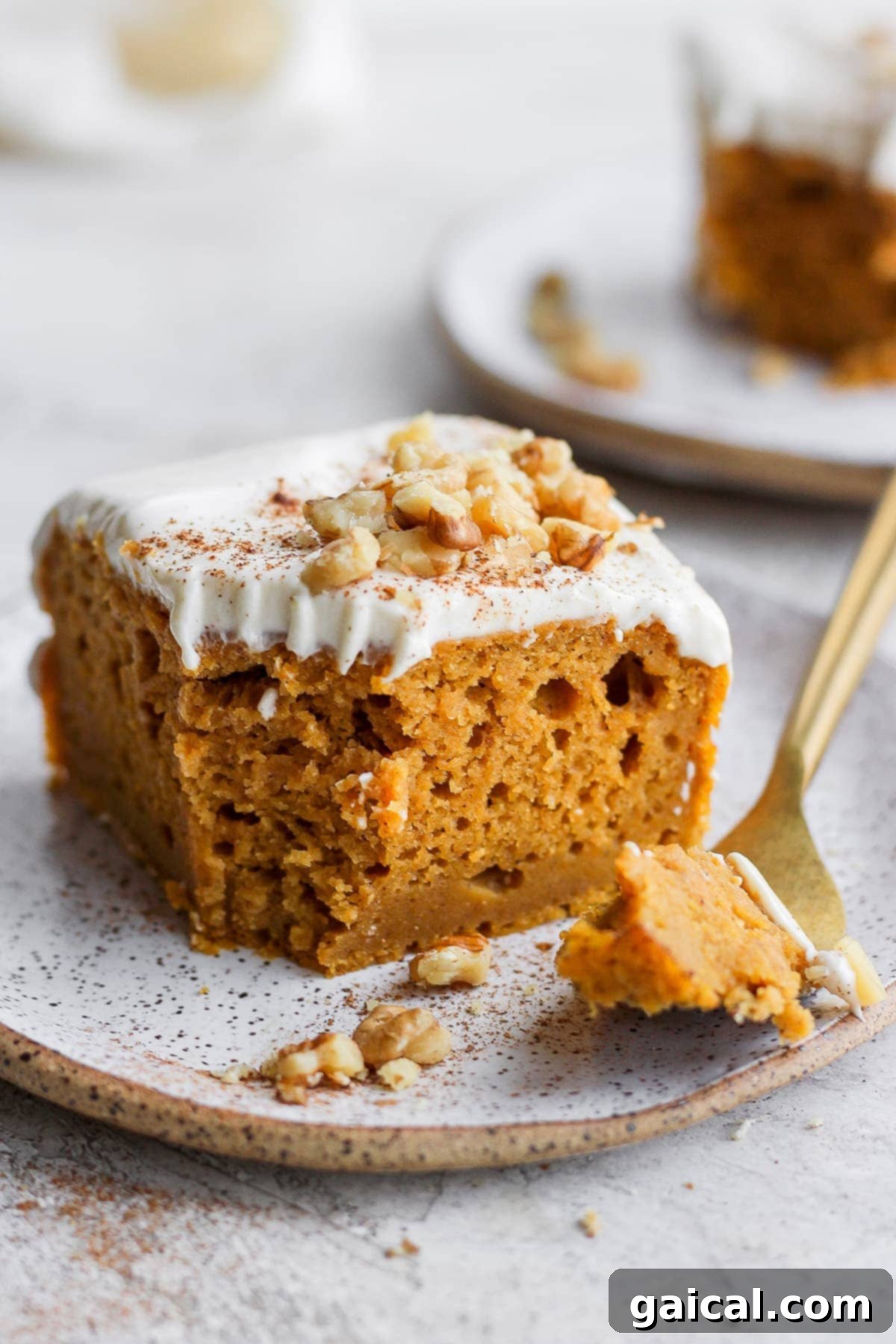 Sheet Pan Pumpkin Perfection 7 A fork holding a bite-sized piece of pumpkin sheet cake, showing the moist interior and frosting, on a plate.