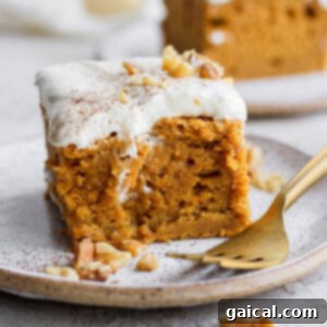 A slice of moist pumpkin sheet cake with generous cream cheese frosting on a plate.