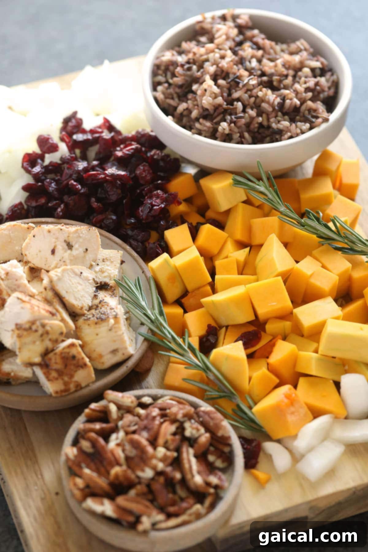 Ingredients for Butternut Squash Wild Rice Casserole laid out and ready to be combined, including diced squash, chicken, wild rice, and fresh herbs.