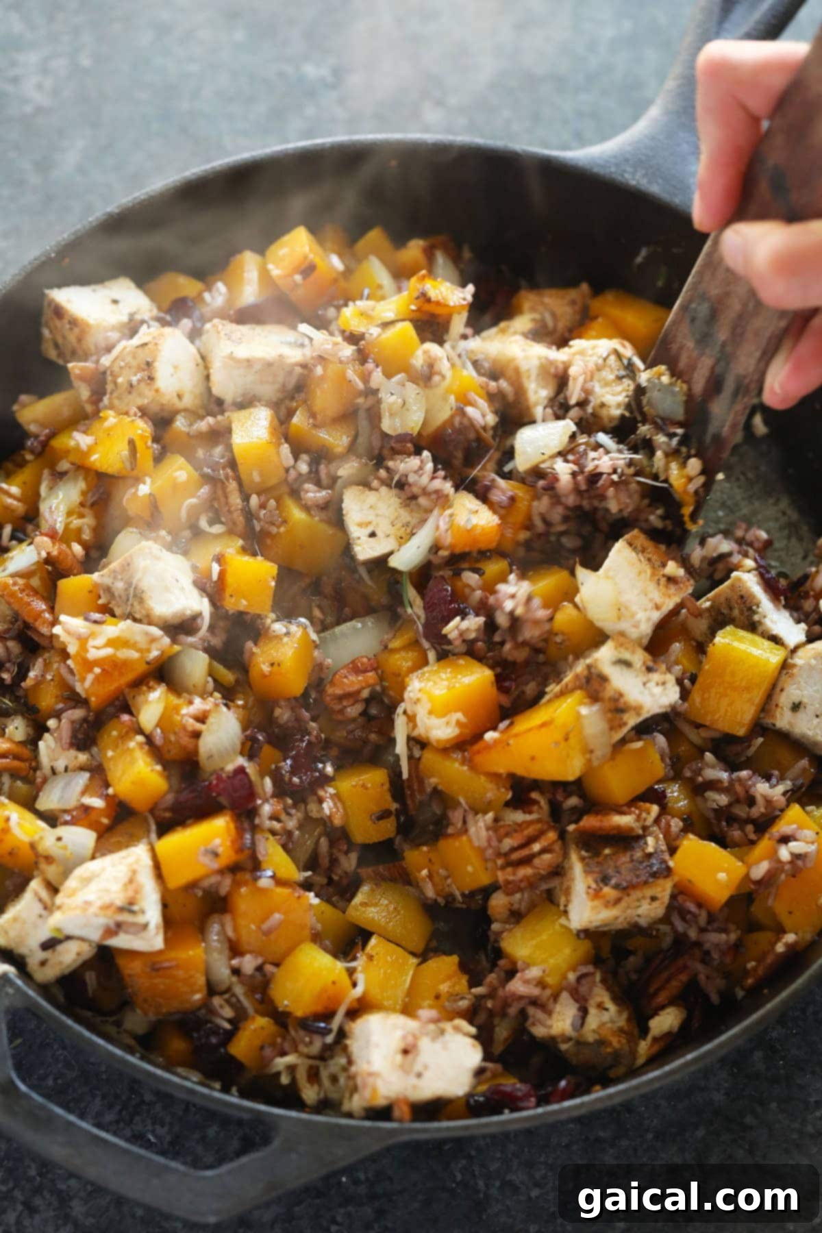 A close-up of Butternut Squash Wild Rice Casserole ingredients being mixed in a large cast iron pan, highlighting the textures and vibrant colors.