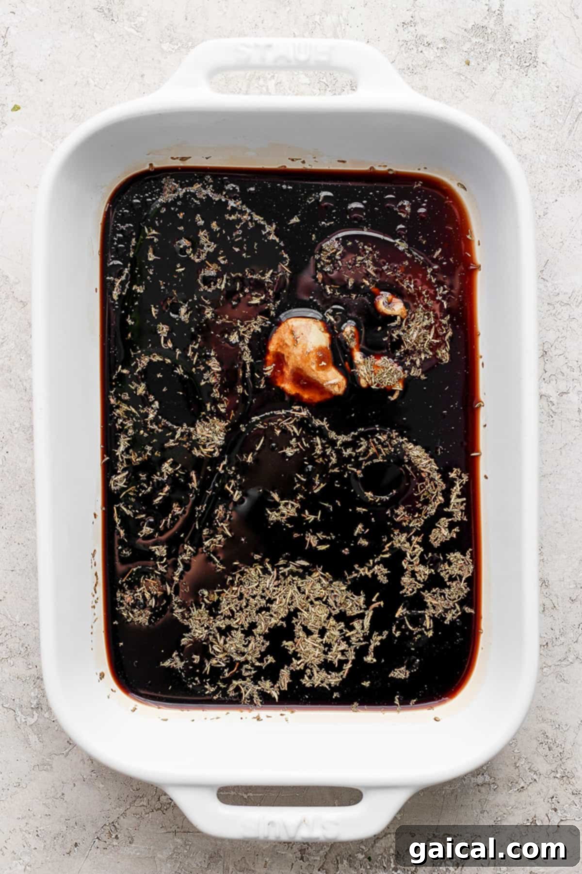 A white ceramic baking dish filled with a rich, dark balsamic marinade sauce, ready for chicken.