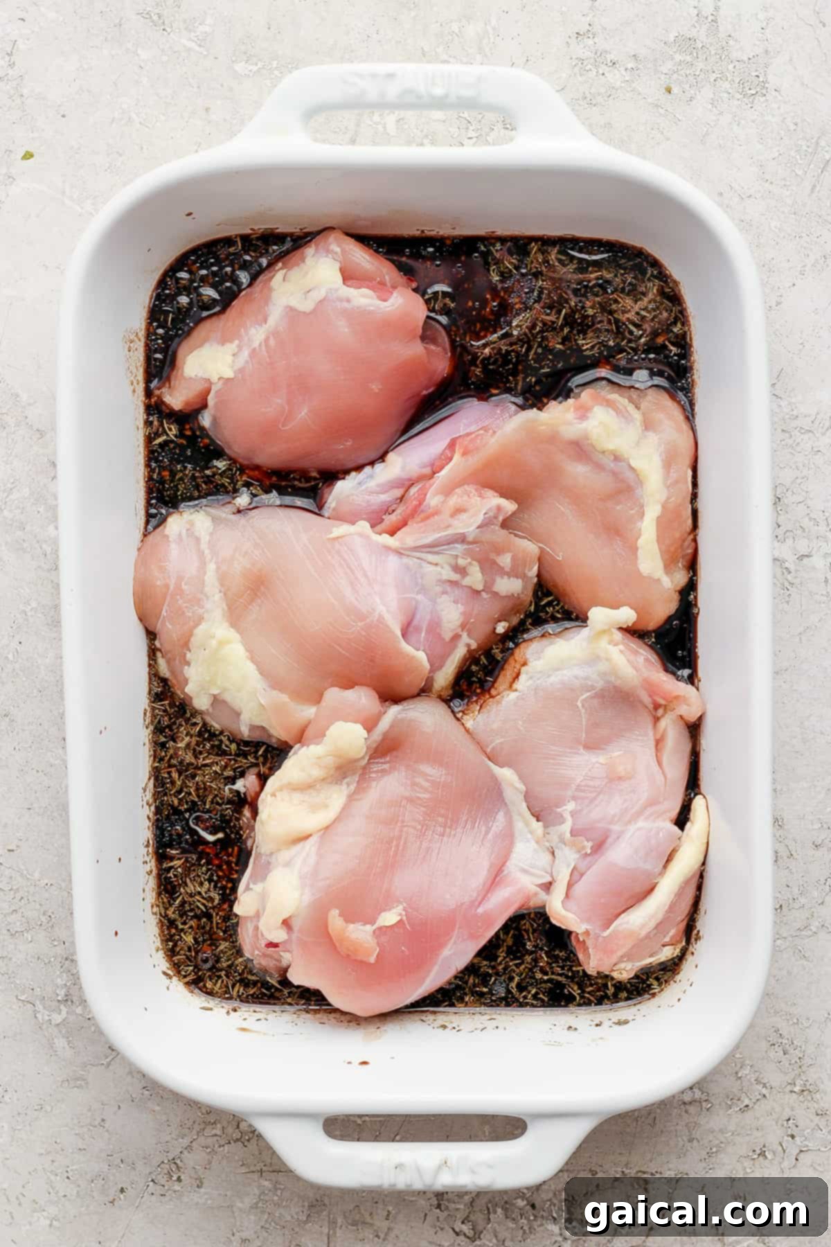 Raw chicken breasts soaking in a rich balsamic marinade in a clear glass baking dish, ready to be refrigerated.