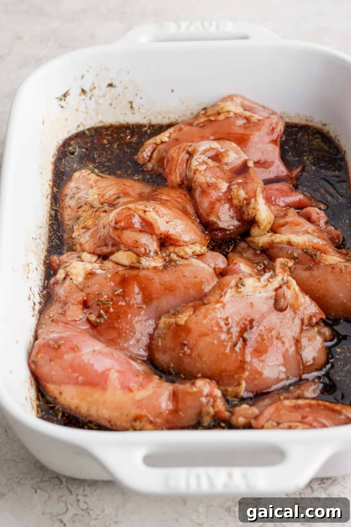 Cooked balsamic chicken breasts glistening with sauce in a white ceramic baking dish.