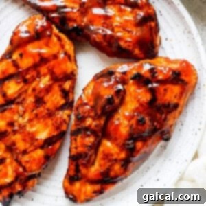 Grilled chicken breasts on a white plate with sauce drizzled over them.