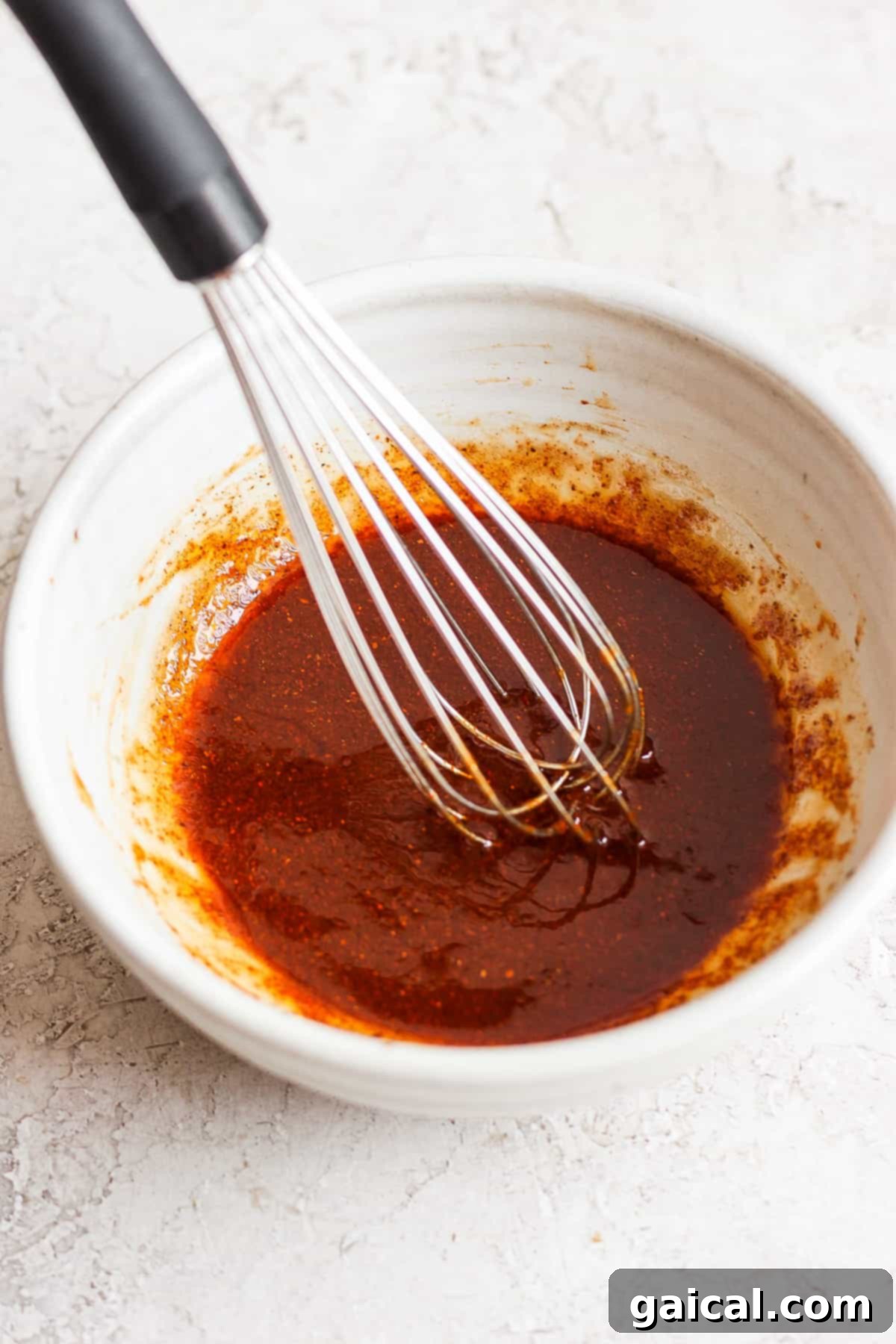 A bowl of the rich, savory BBQ chicken marinade with a whisk inside.