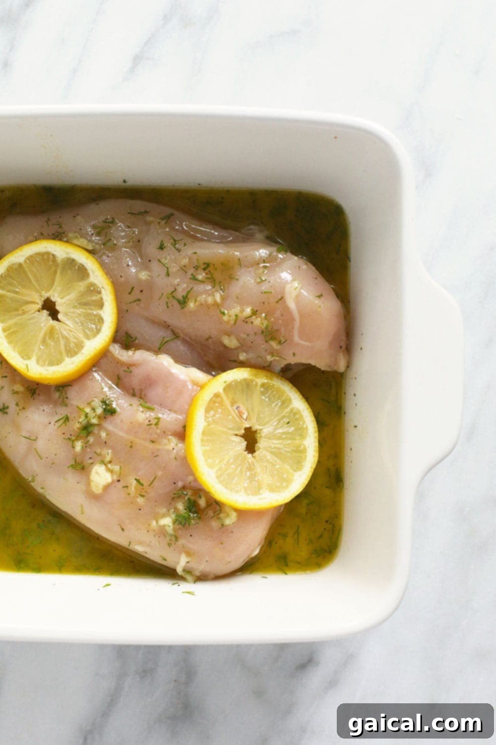 Raw chicken breasts generously coated in a bright yellow lemon chicken marinade, ready for cooking in a baking dish.