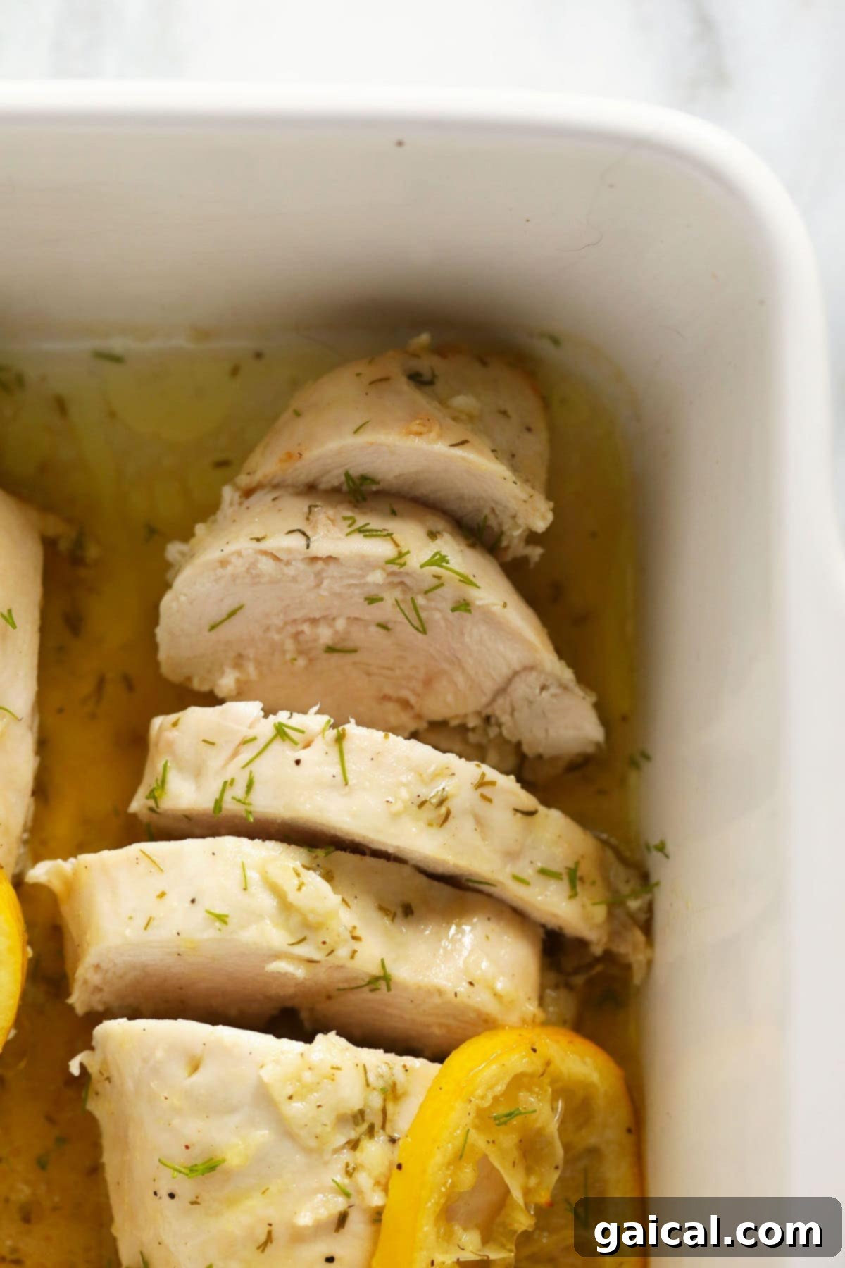 Perfectly cooked and sliced lemon chicken breasts arranged in a baking dish, garnished with fresh herbs.