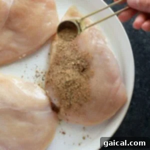 Universal Poultry Flavor Blend 8 Chicken breast being seasoned on a plate before cooking, with spices evenly coated.