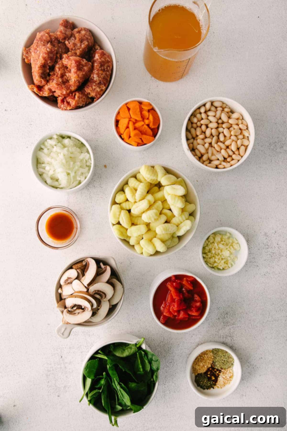 Individual bowls containing prepped ingredients for sausage gnocchi soup, including sliced mushrooms, diced carrots, and fresh spinach.