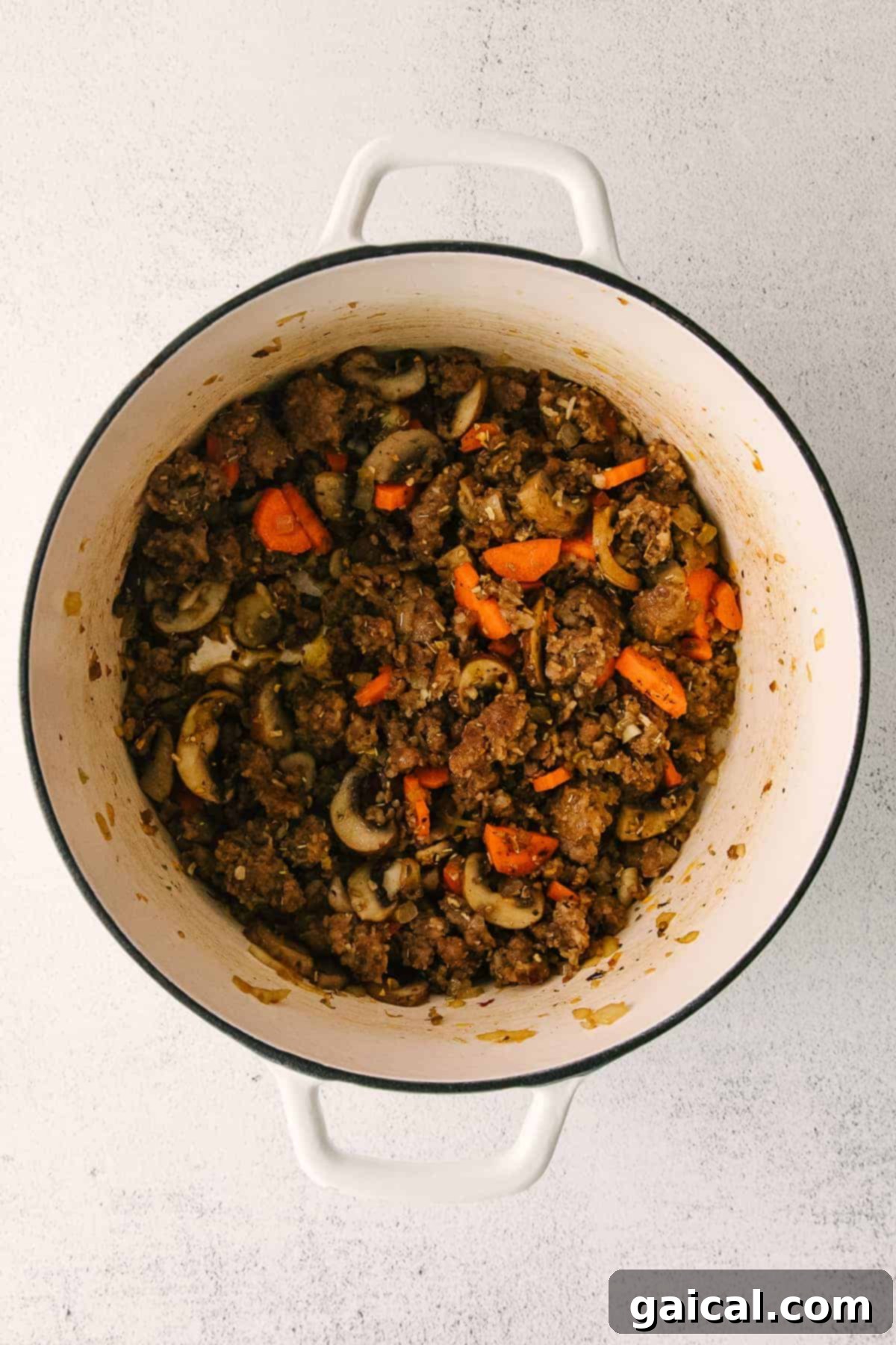 Sausage gnocchi soup simmering in a large stock pot on the stove, showing the vibrant colors of the ingredients.